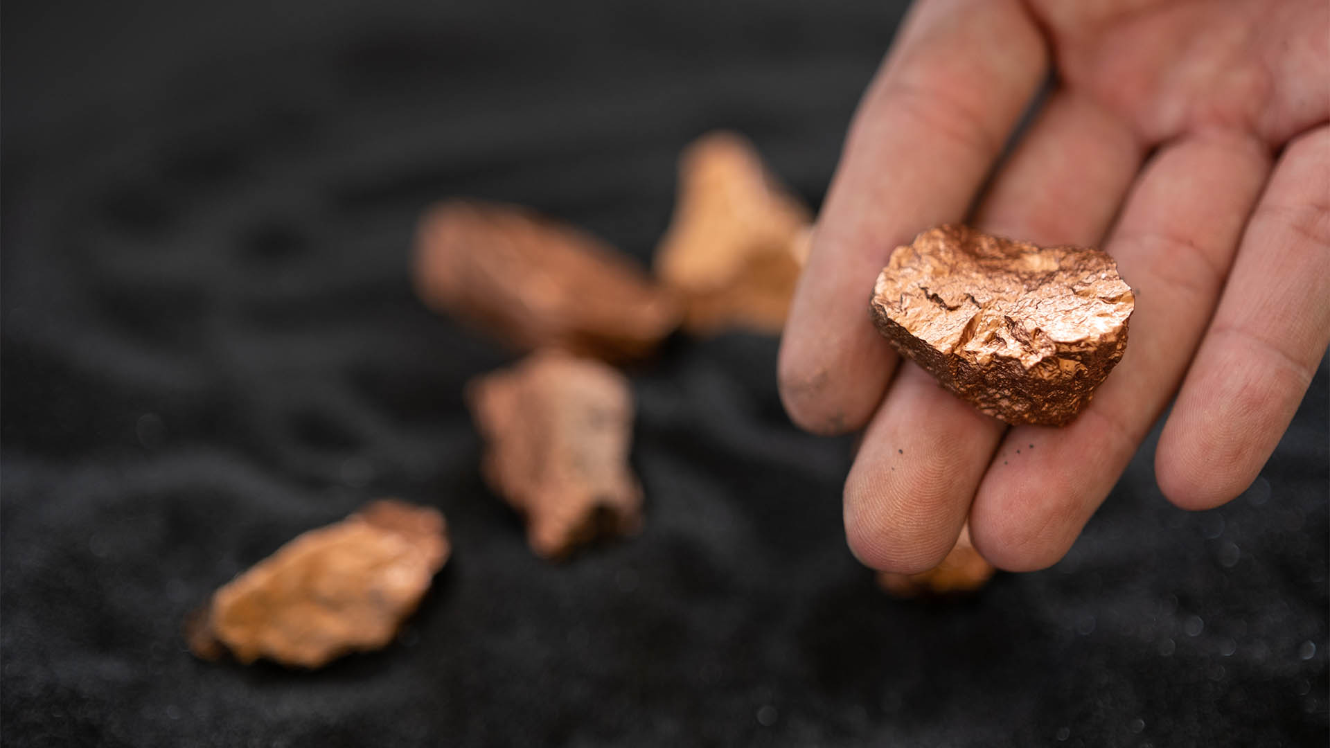 Man's hand holding a piece of copper to examine it for industrial use on black background
