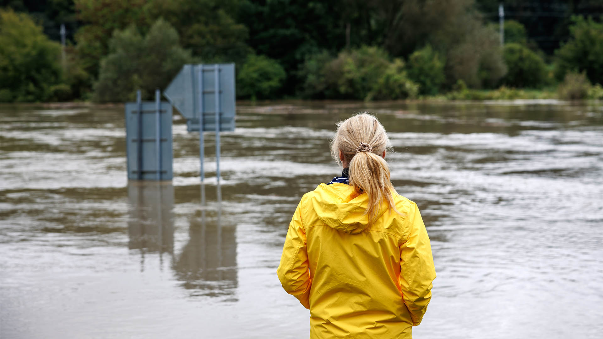 Flooded river. Worried woman looking at overflowing water during flood. Extreme weather and natural disaster