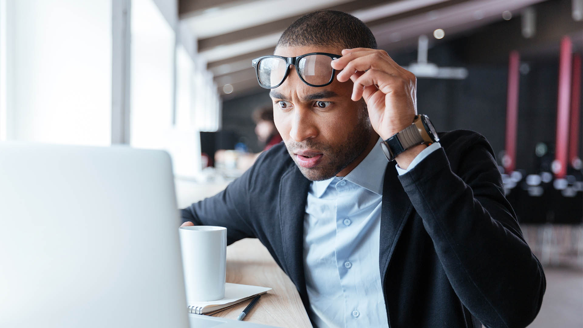 Businessman receiving negative news, touching his glasses, being mad, upset and surprised in front of laptop