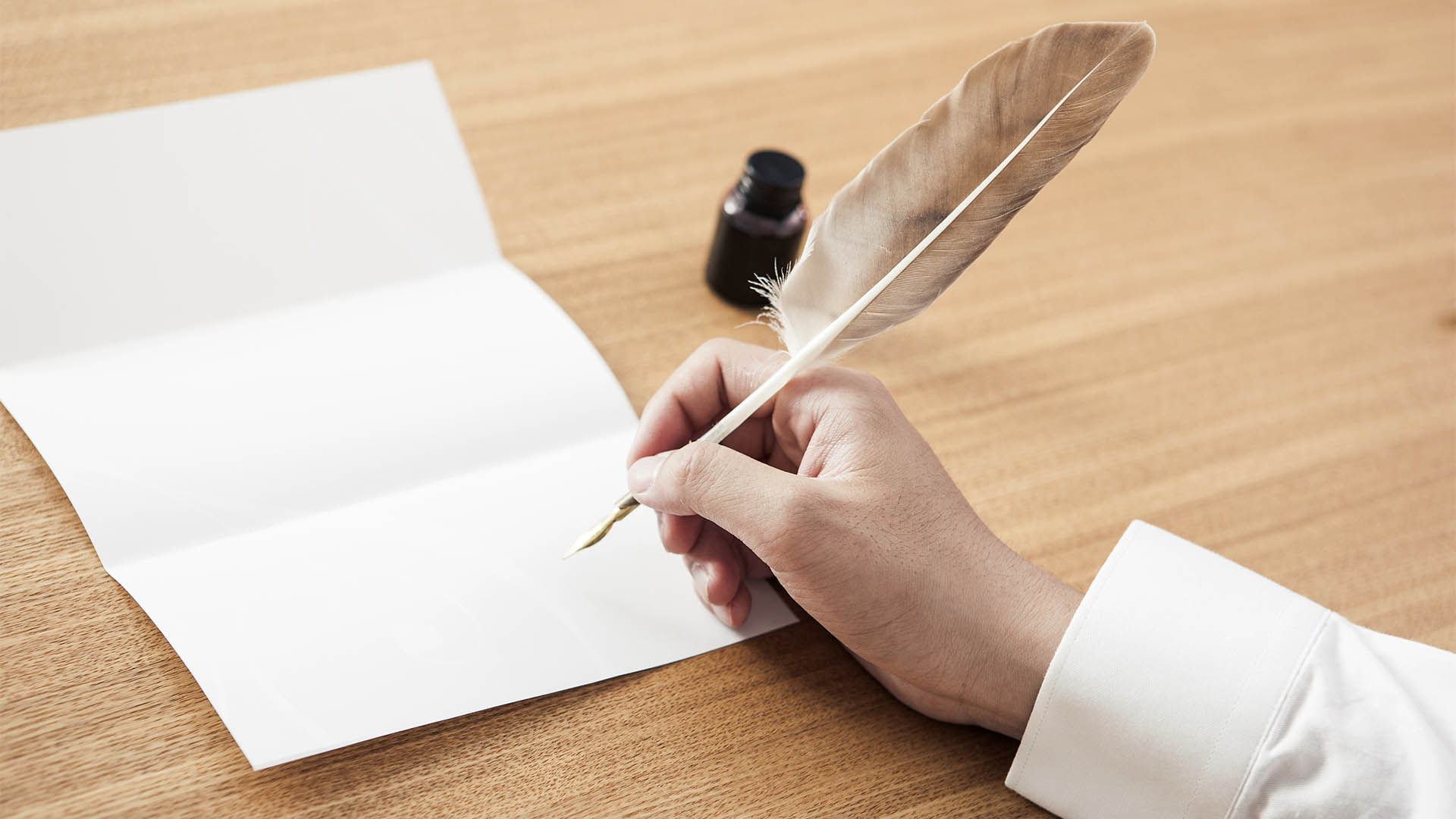 A man hand hold a fountain pen and write with blank letter on the wood table(desk)