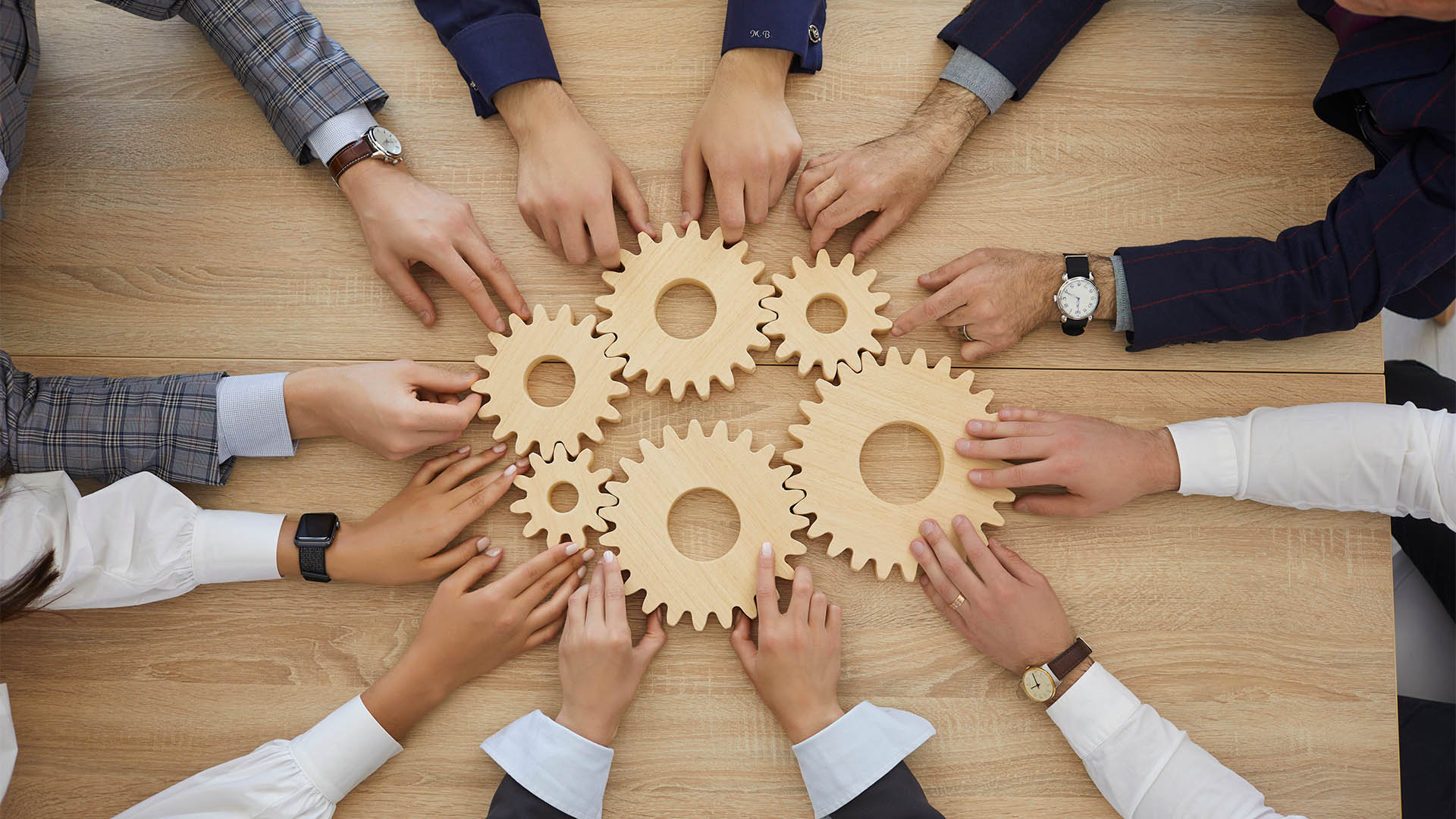 Top view of hands of business people stacking wooden gears next to each other which symbolizes development, teamwork and success. Concept of business cooperation and the corporate community. Close up.