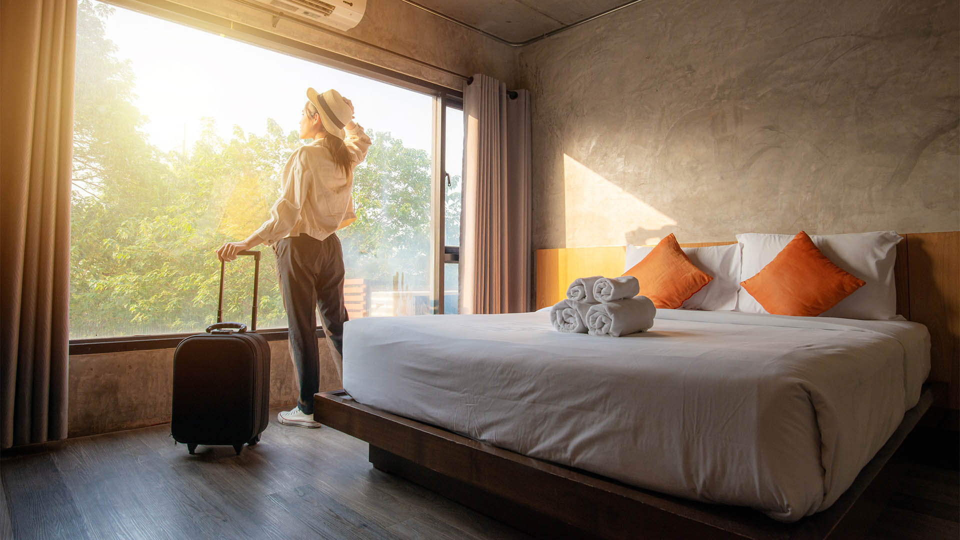 Portrait of tourist woman standing nearly window, looking to beautiful view with her luggage in hotel bedroom after check-in. Conceptual of travel and vacation.