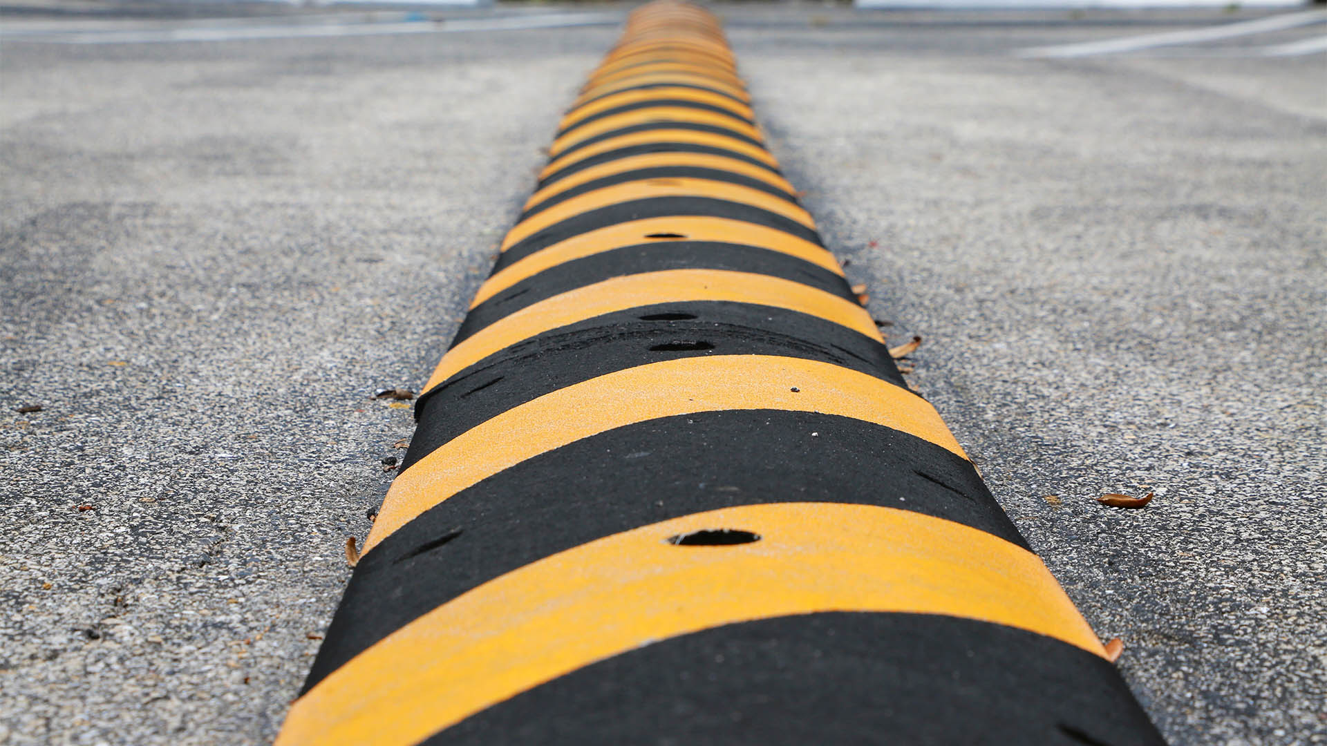 Yellow and Black Striped Speed Bump with Nails Visible in Parking Lot with Diagonal Spaces, White Blocks and Green Grass Above in Background
