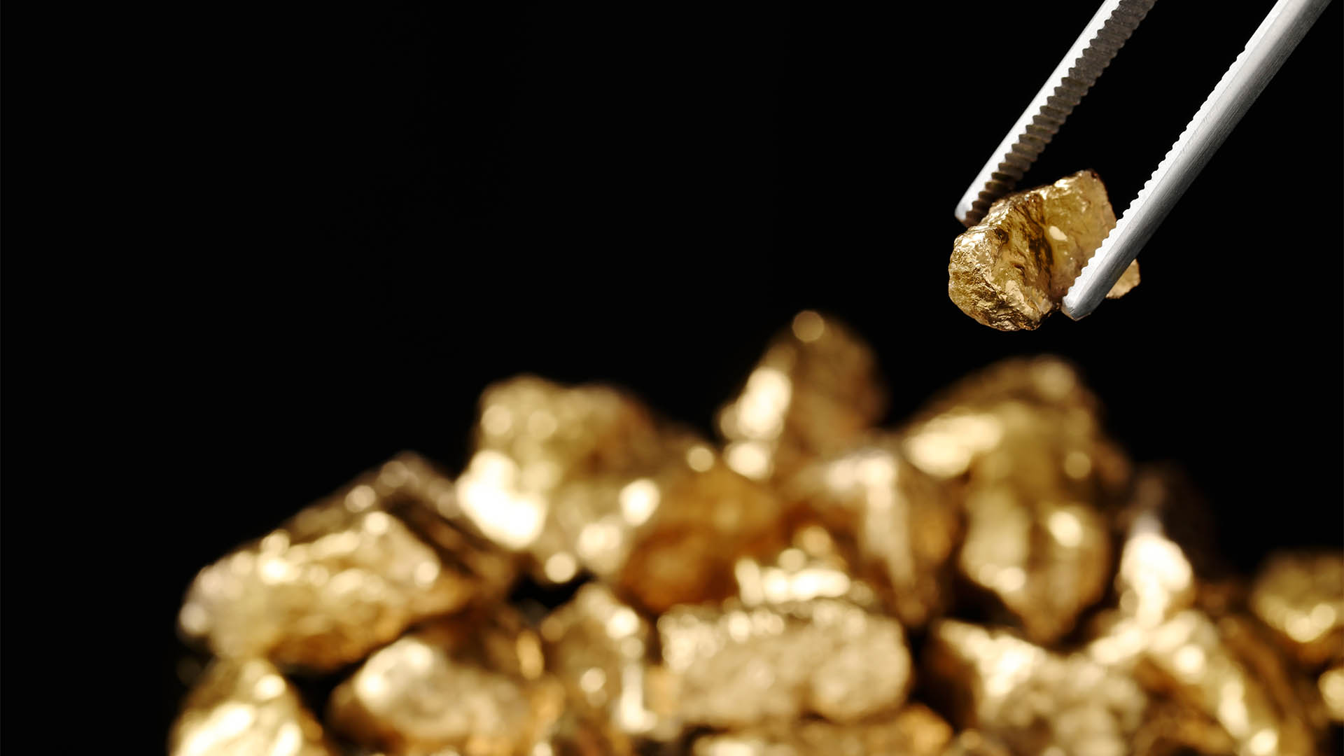 Tweezers with gold nugget against blurred background, closeup. Space for text