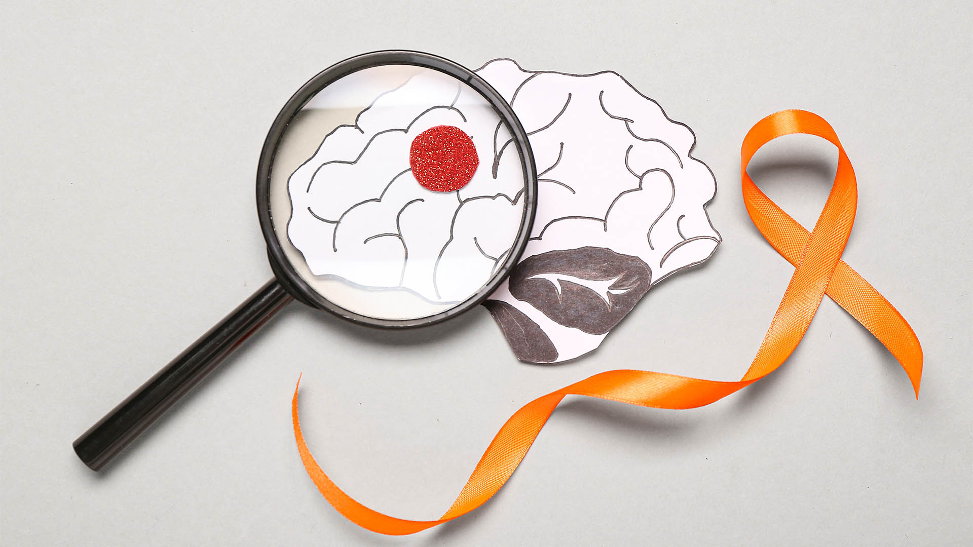 Orange ribbon, paper brain and magnifying glass on grey background. Multiple Sclerosis Awareness Month