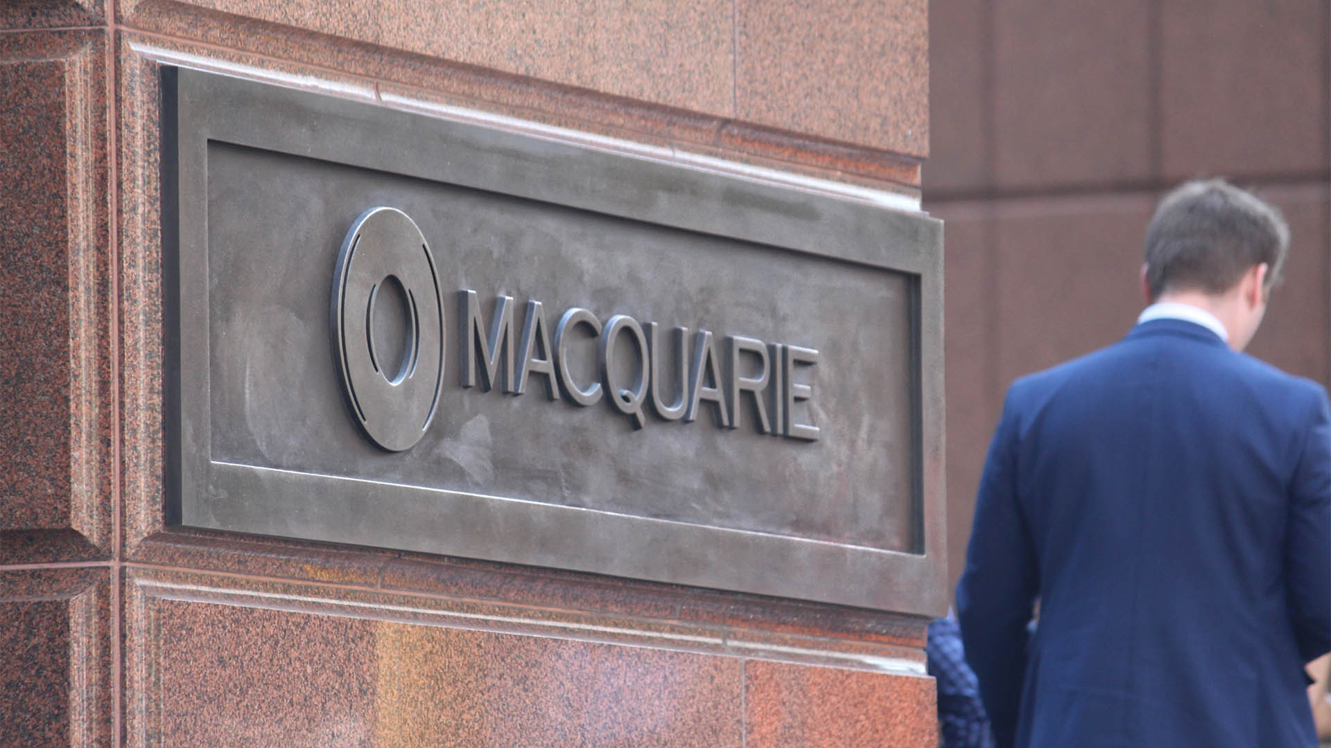 Sydney, NSW Australia - March 12 2021: Plaque with the Macquarie Bank Limited logo on it. The plaque is on the exterior of a building in Martin Place. A man in a suit is waking by