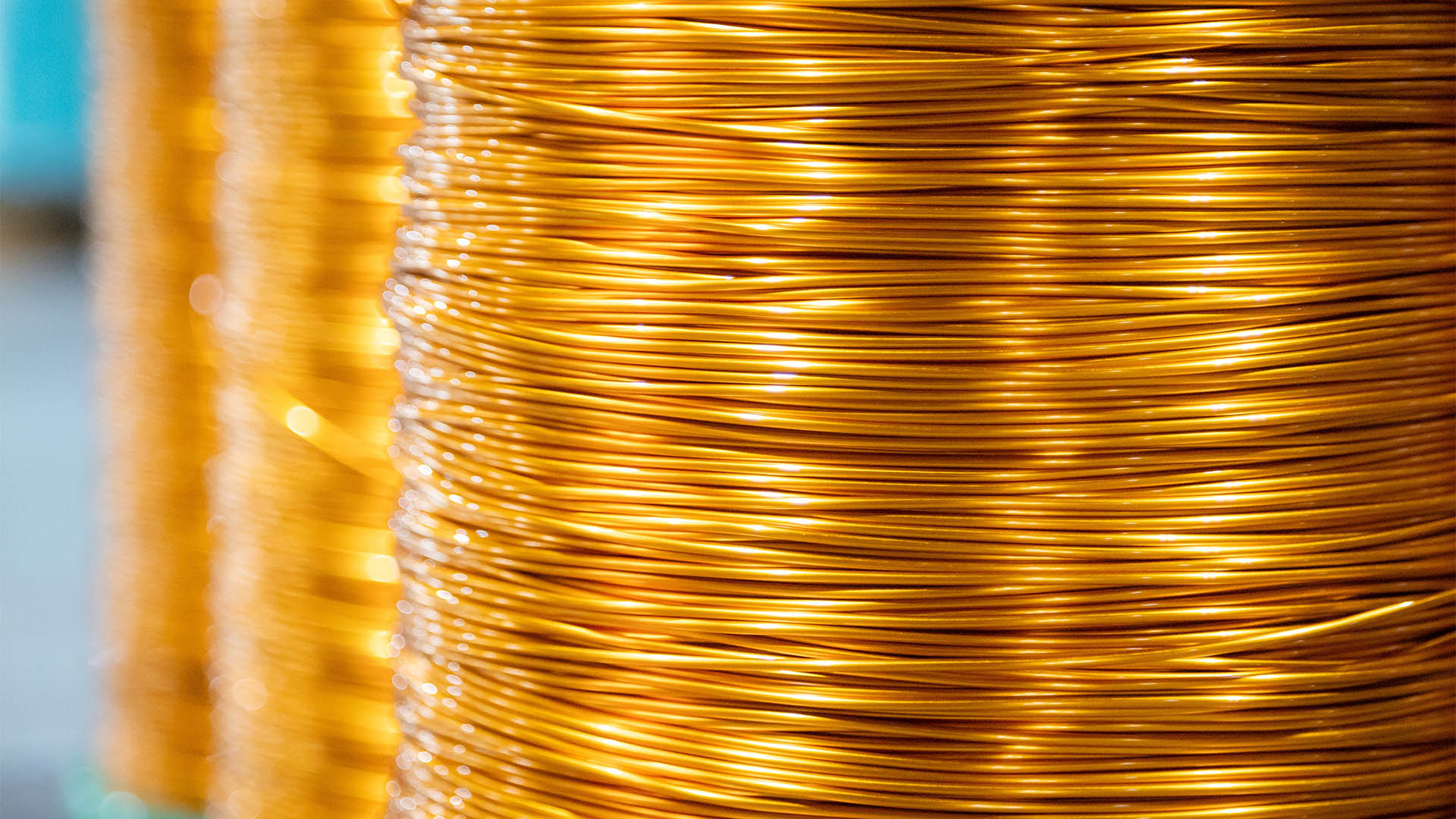 Close-up view of neatly wound copper wire coils in a manufacturing environment. The image highlights the vibrant metallic sheen of the copper against a blurred industrial background