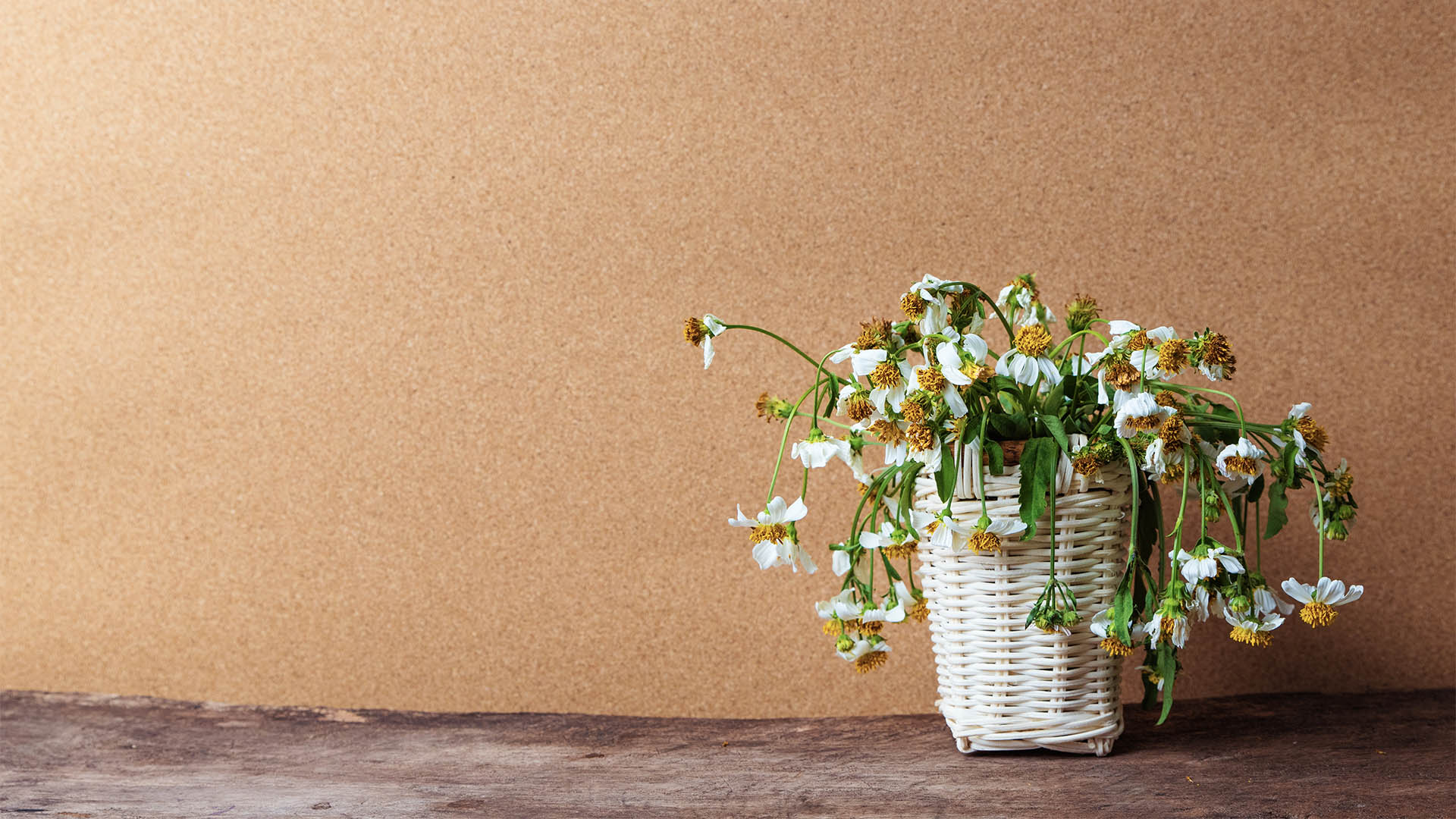 white flowers in basket on wooden table with brown paper background, vintage tone.