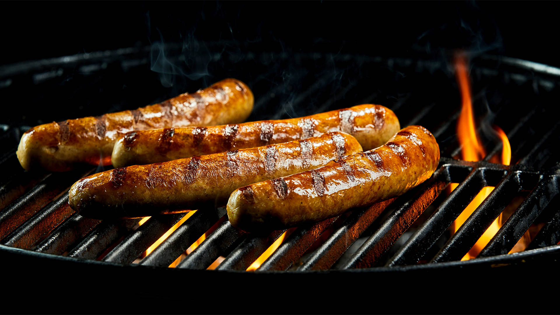 Tasty sausages sizzling on a portable BBQ fire grilling over the flames on a summer picnic, close up view