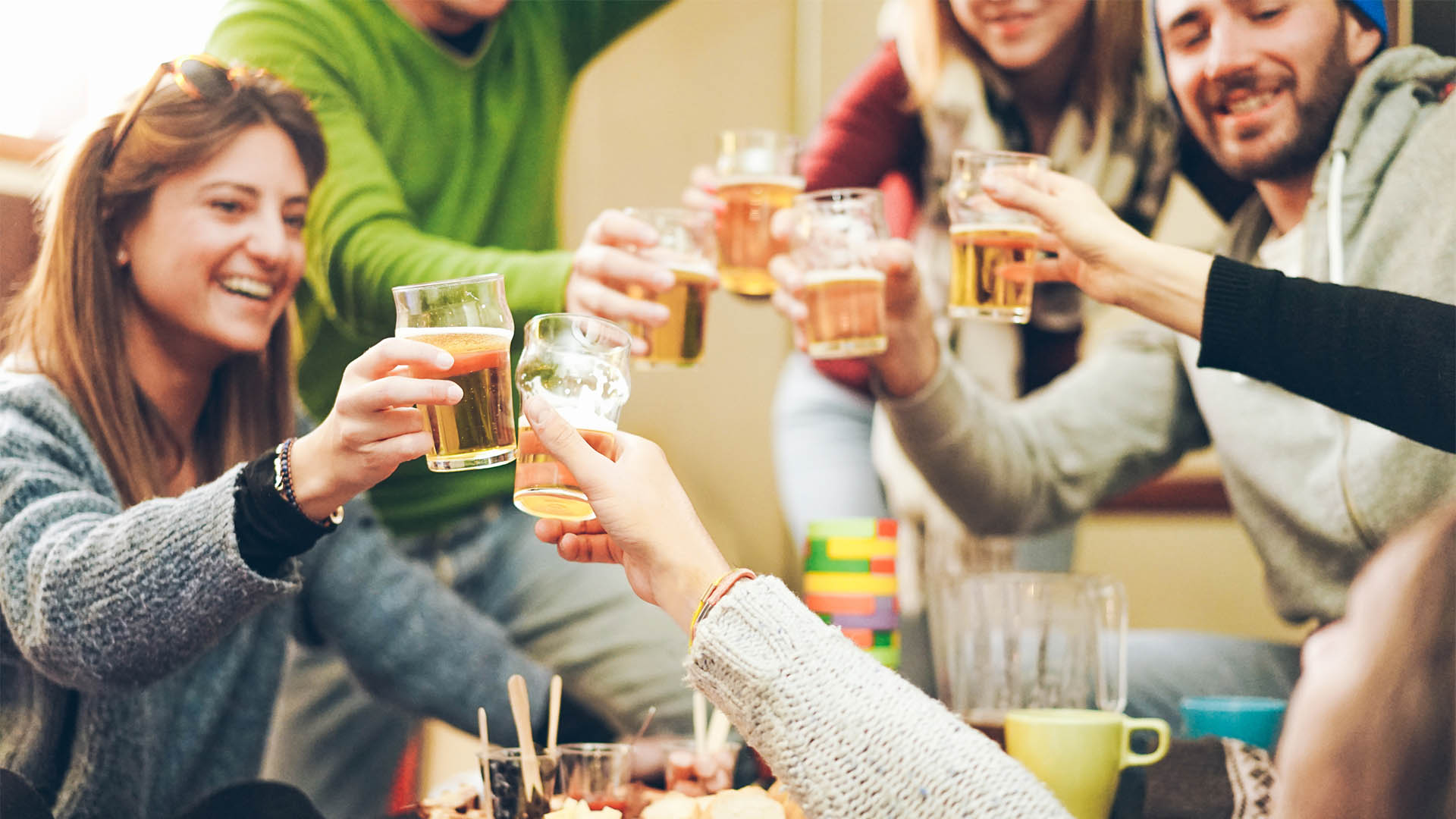 Group of happy friends cheering with beer after skiing day in bar pub restaurant - Young people toasting appetizer in brewery chalet - Concept about good and positive mood - Focus on right bottom hand