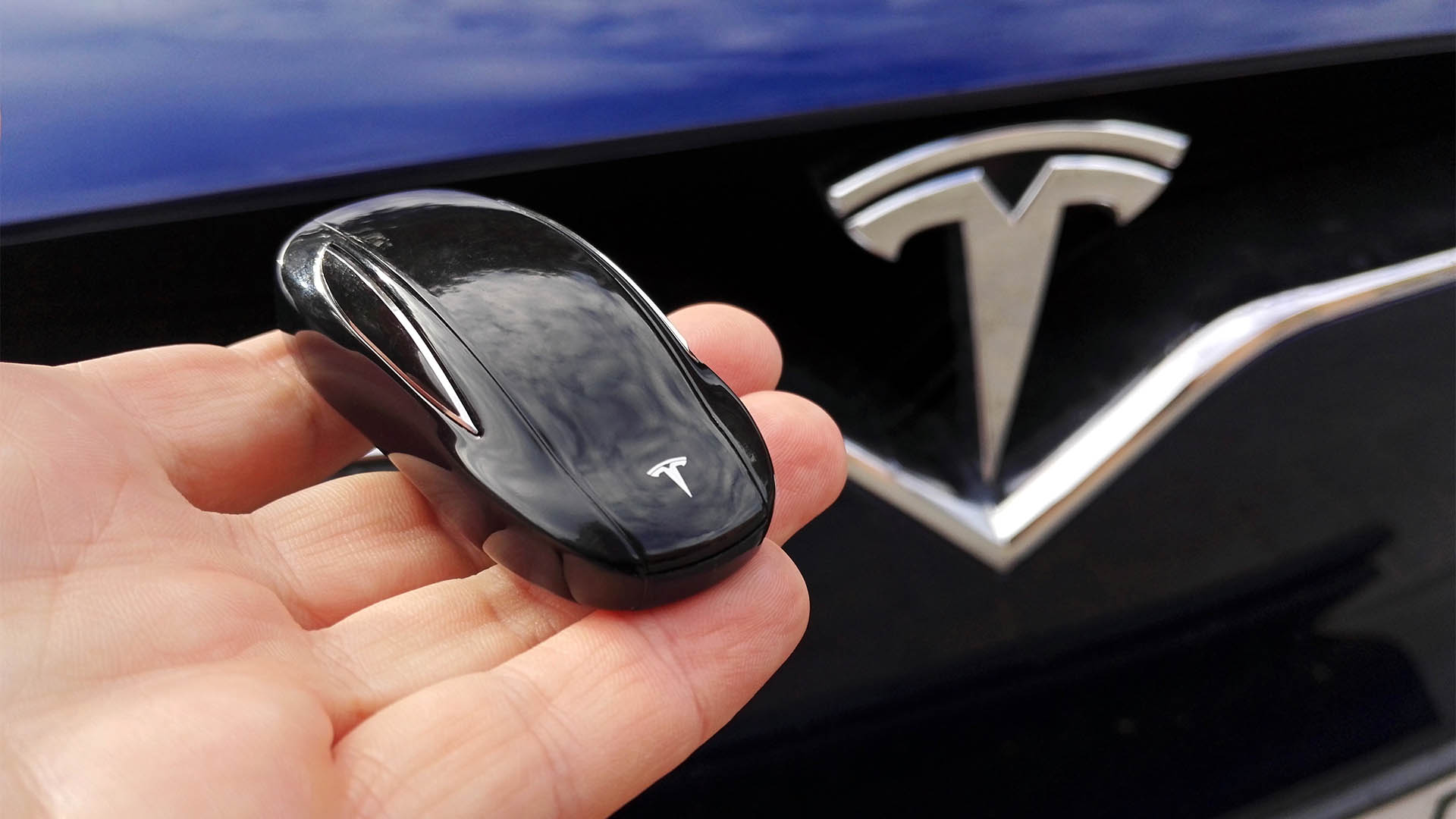 Poznan, Poland - September, 13, 2017: Key for Tesla car on hand with Tesla Model X car front with logo in background.