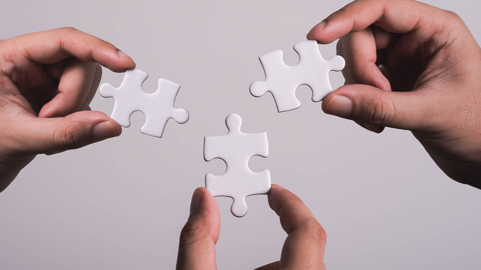 three hands trying to connect couple puzzle piece with gray background. Jigsaw puzzle team work concept. one part of whole. symbol of association and connection. business strategy.