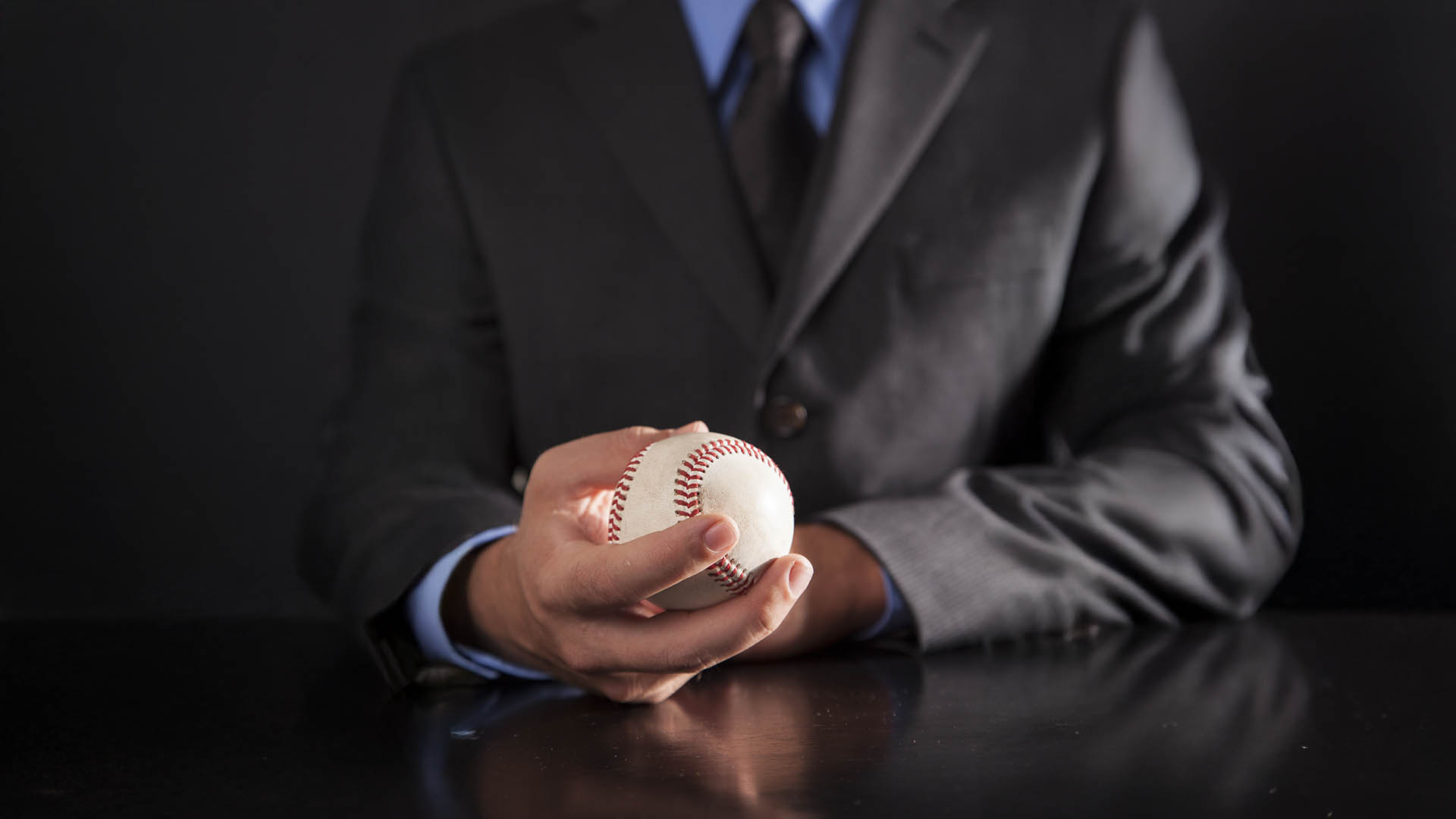A young executive sits at his desk holding a baseball.