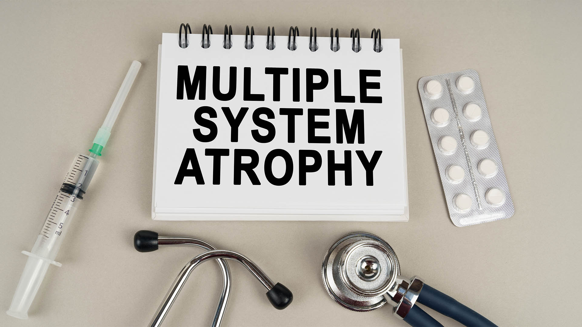 Medical concept. On a gray surface, a syringe, a thermometer, a stethoscope, a blister and a notepad with the inscription - Multiple system atrophy
