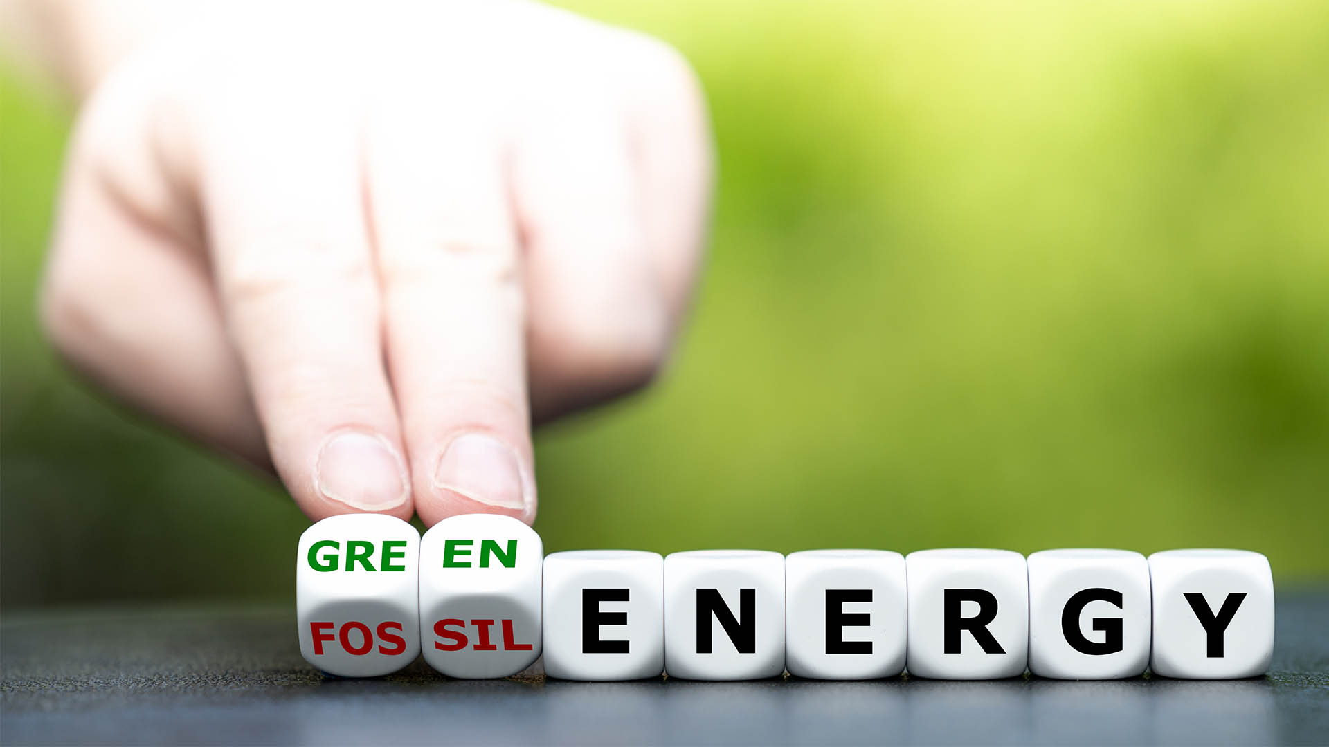 Hand turns dice and changes the expression "fossil energy" to "green energy".